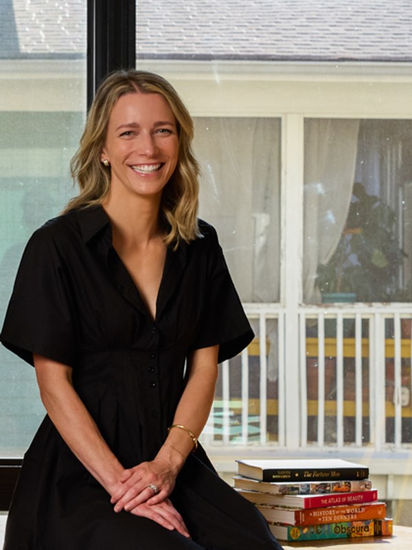 Kate seated on the edge of a long oak library table with a stack of vintage books beside her and a bright window behind