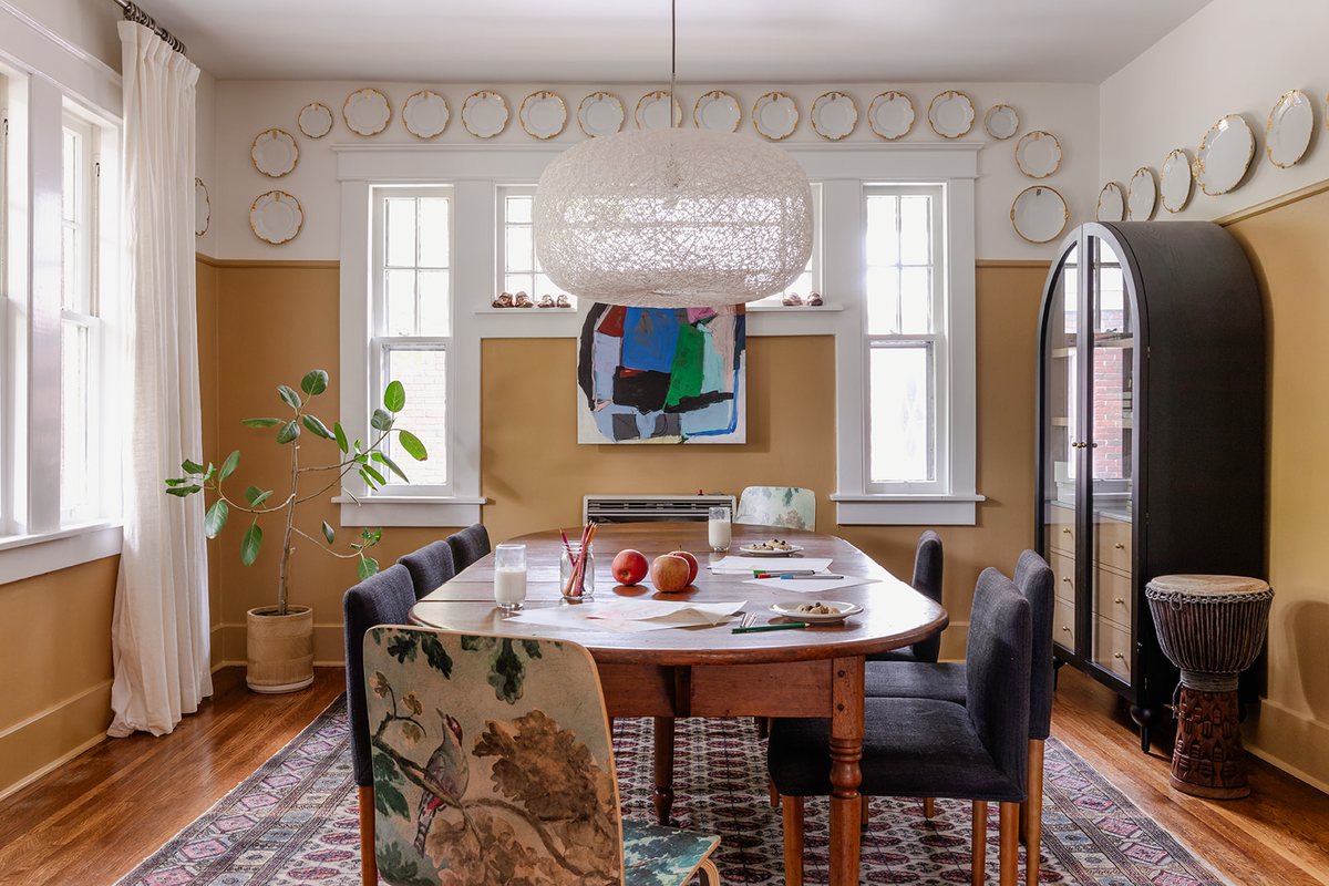 A dining room with a vintage oval table, mixed chairs, a plate wall, and a woven pendant light